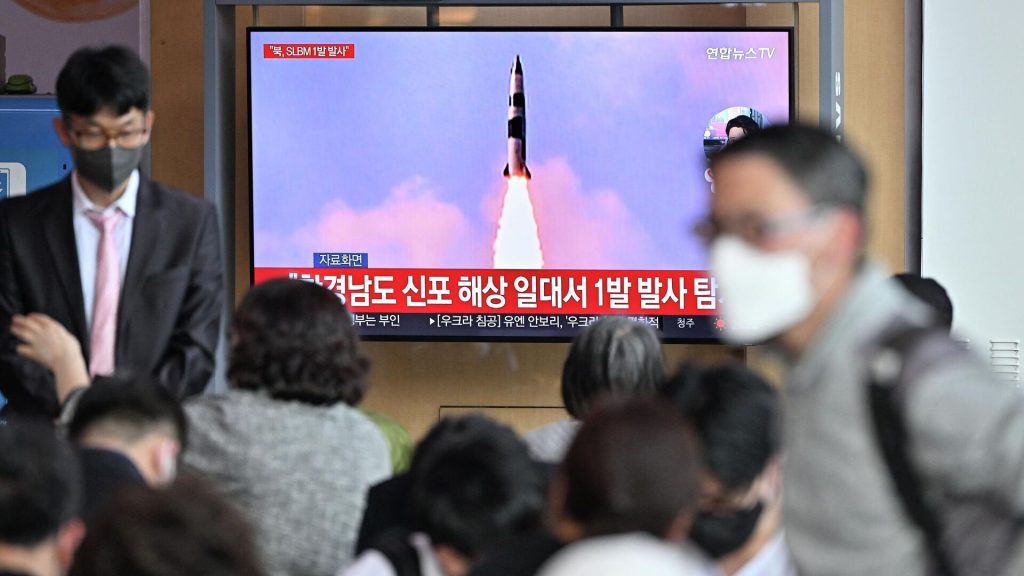 Люди возле экрана, транслирующего репортаж о запуске КНДР баллистической ракеты